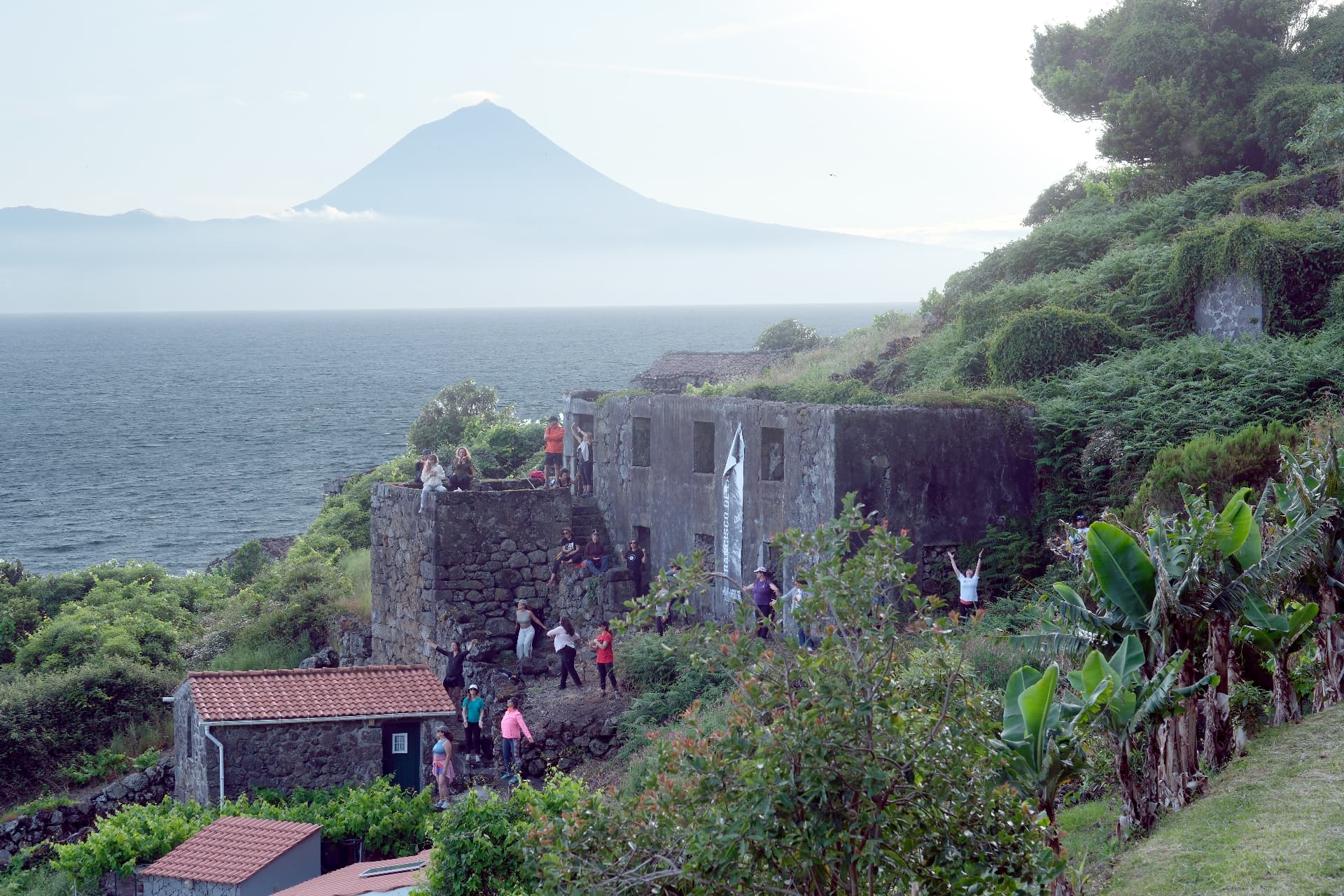 Grupo em ruínas de pedra na costa de São Jorge com o Pico ao fundo