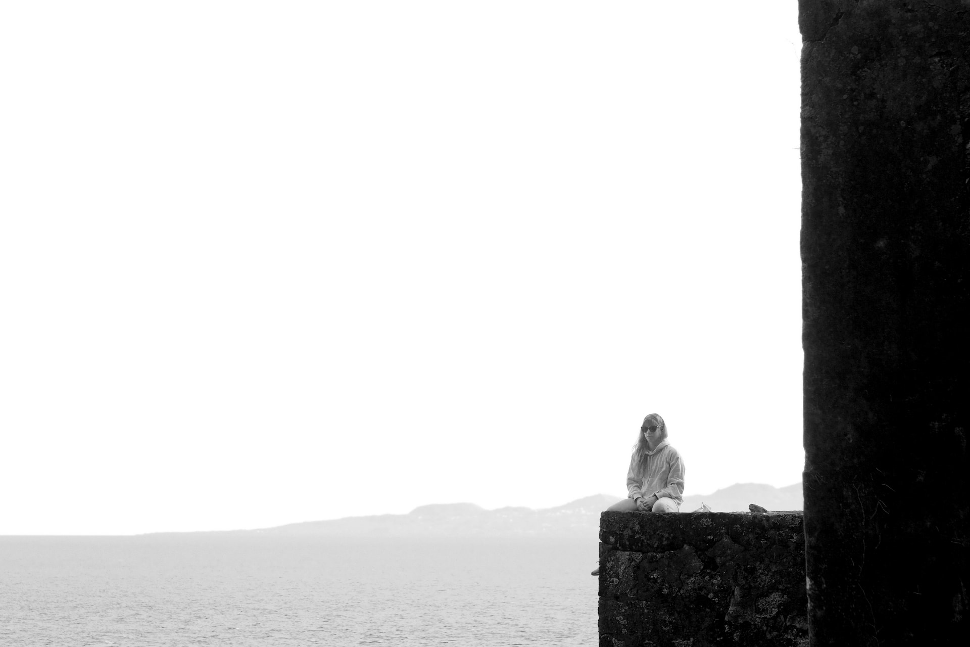 Participante sentada num muro de pedra frente ao mar, a preto e branco